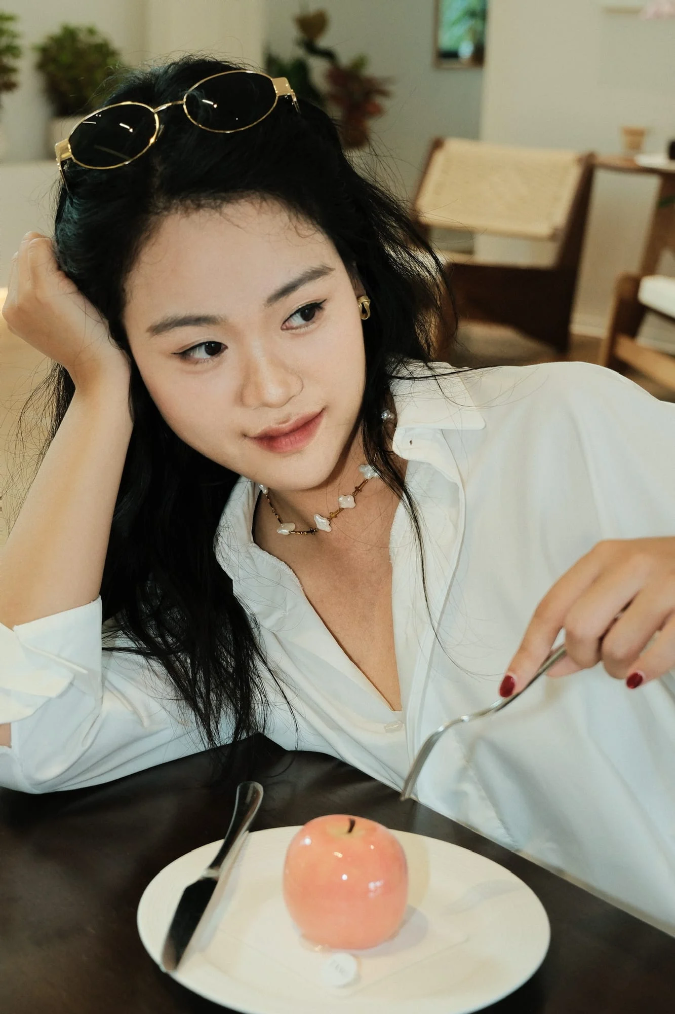 The cross choker worn by a model in a white shirt resting her chin on her hand in front of a dessert.