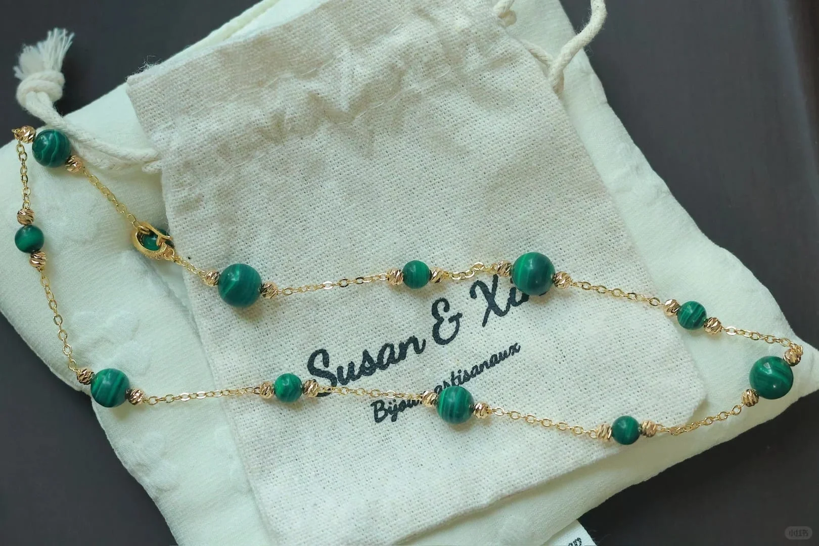 The same malachite station necklace looped over a Susan&Xin pouch, round clasp visible.