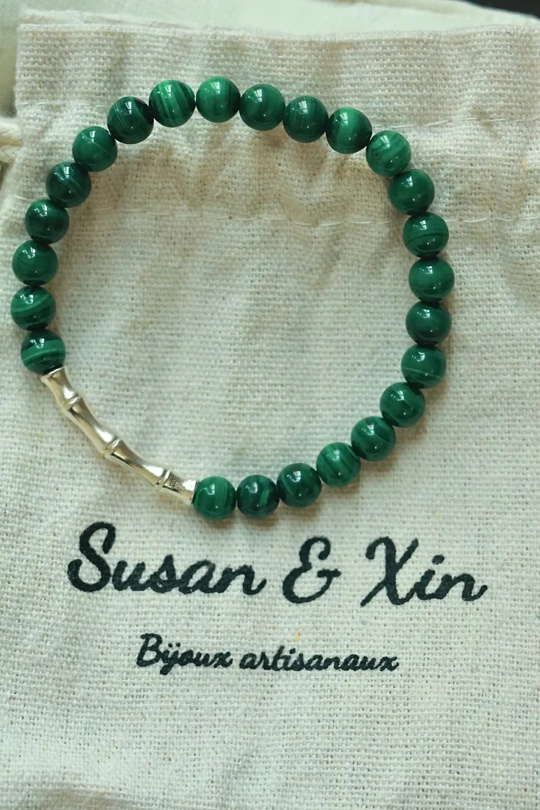 Bracelet of small banded malachite beads with one pale gold-toned bamboo-shaped link, on a Susan&Xin fabric pouch.