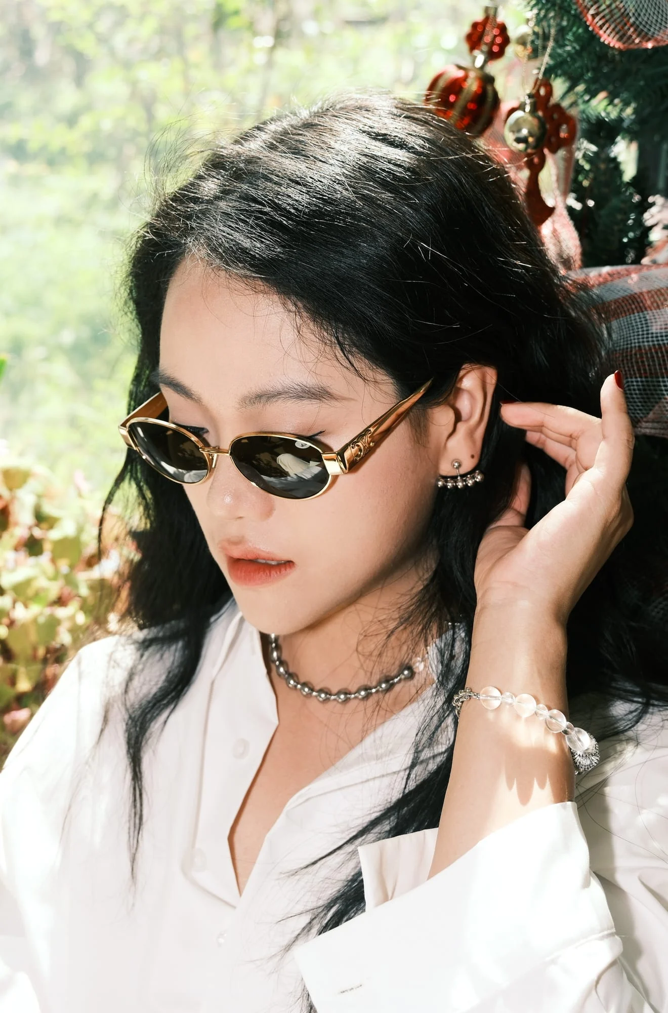 The silver-toned bead choker worn by a model in gold-toned sunglasses beside a Christmas tree.