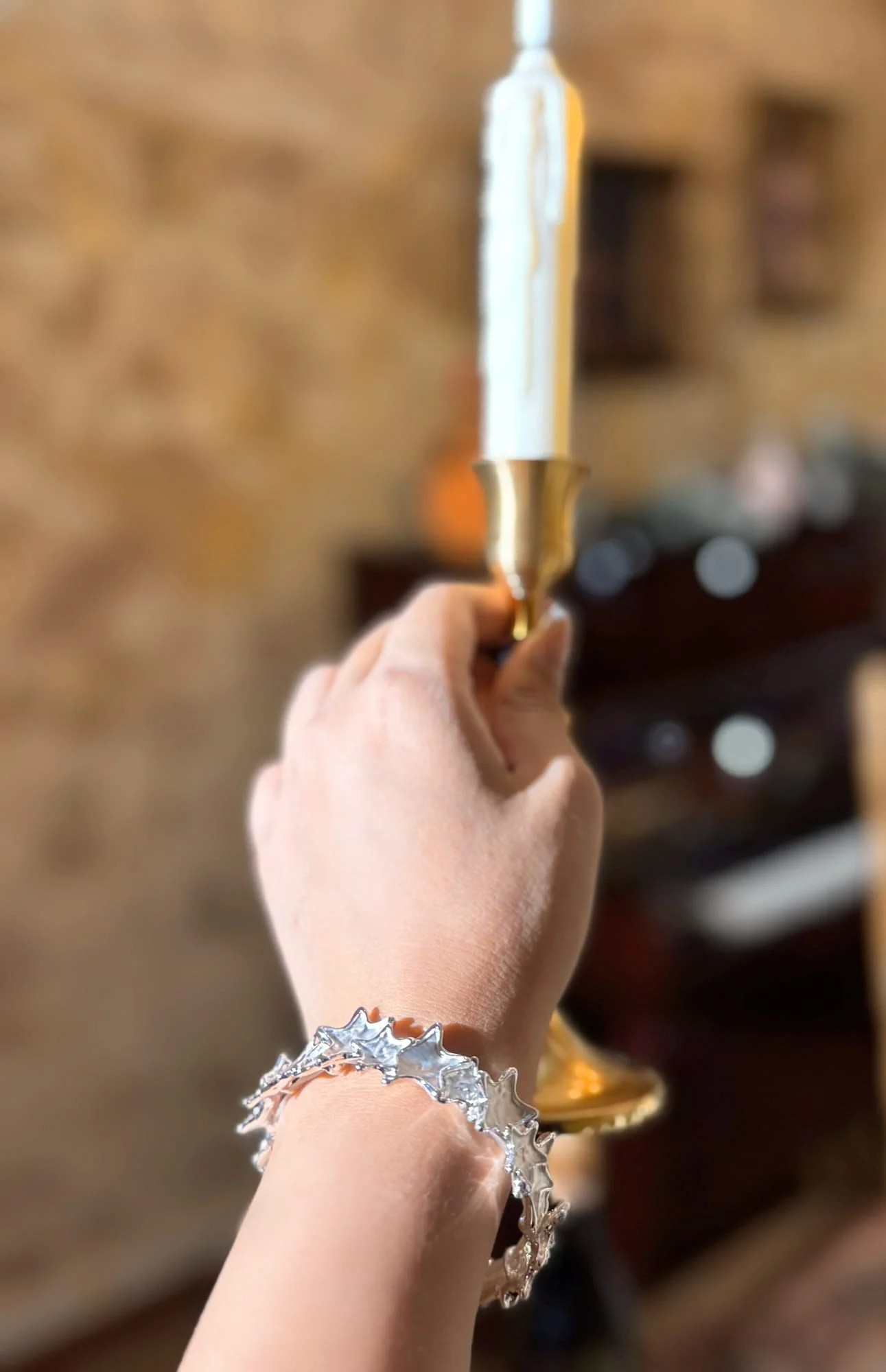 Wrist wearing the silver-toned star bangle, hand raising a brass candlestick with a white candle, background blurred.