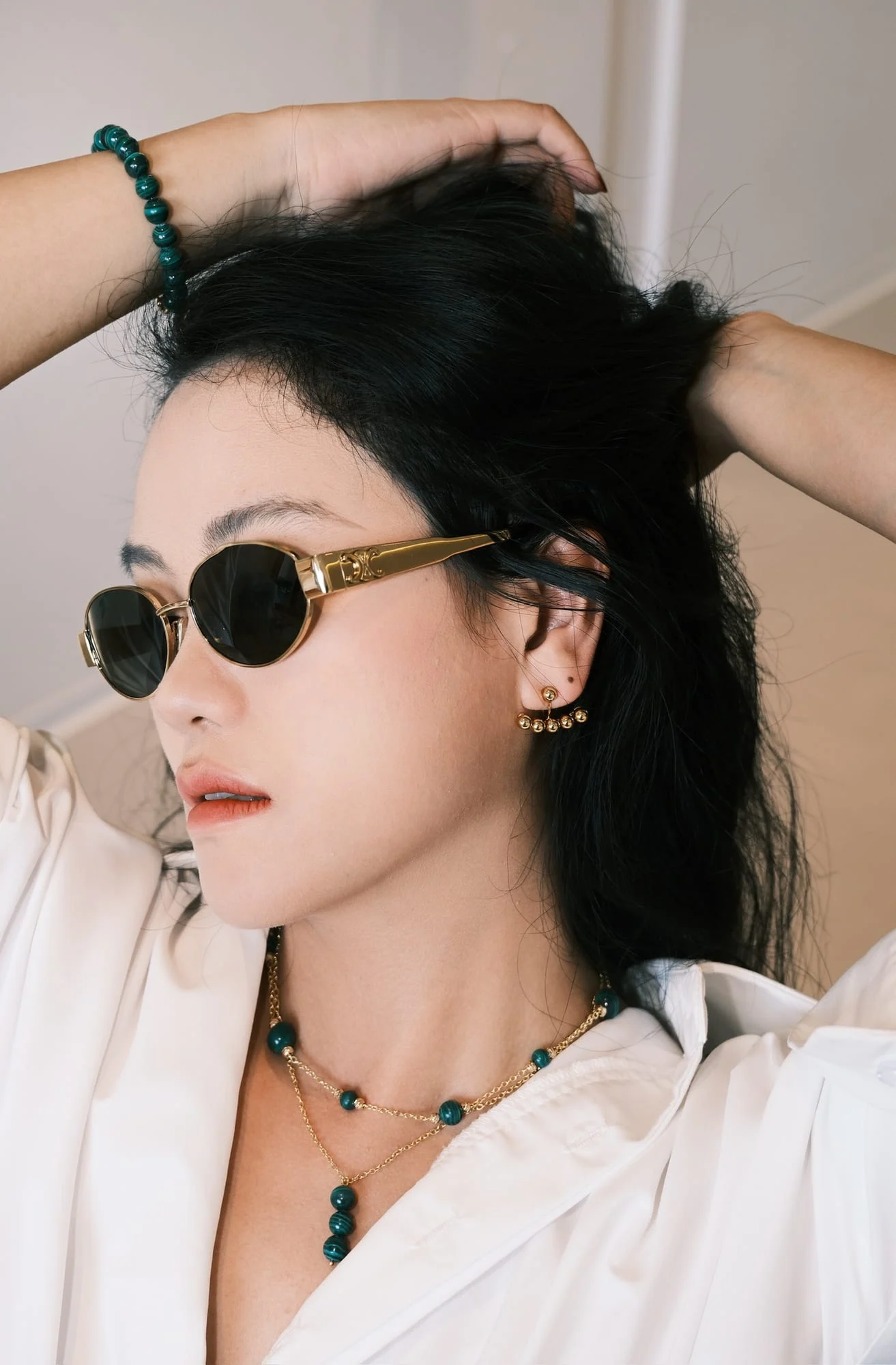 The three-bead drop necklace worn by a model in gold-toned sunglasses lifting her hair, layered with a green-bead station necklace.