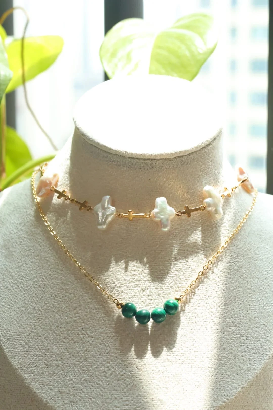 The cross choker on a display bust by the window, layered above the C005 four-bead necklace.