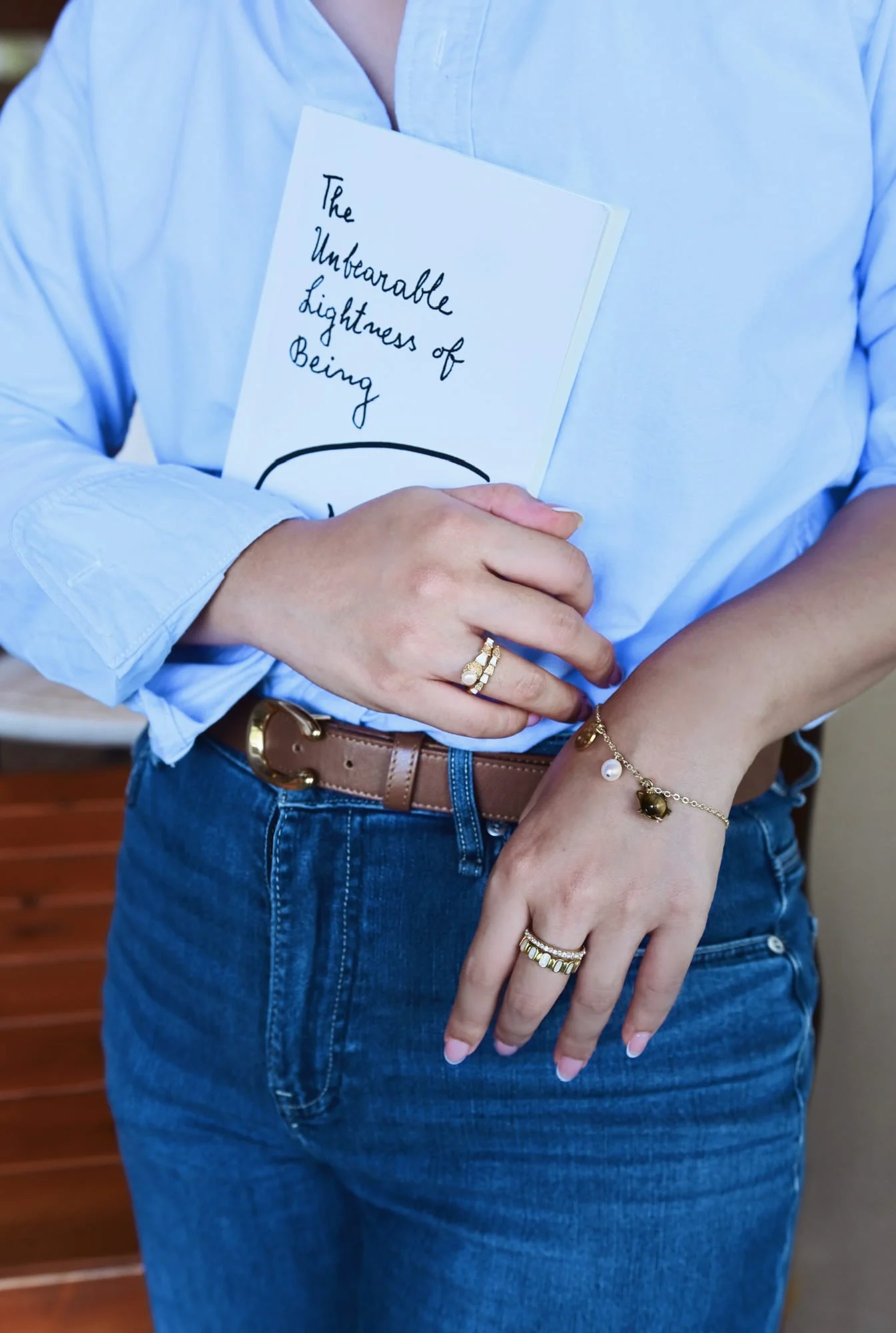 The charm bracelet on the left wrist of a model holding a white-covered book: disc, white bead and brown banded bead charms.