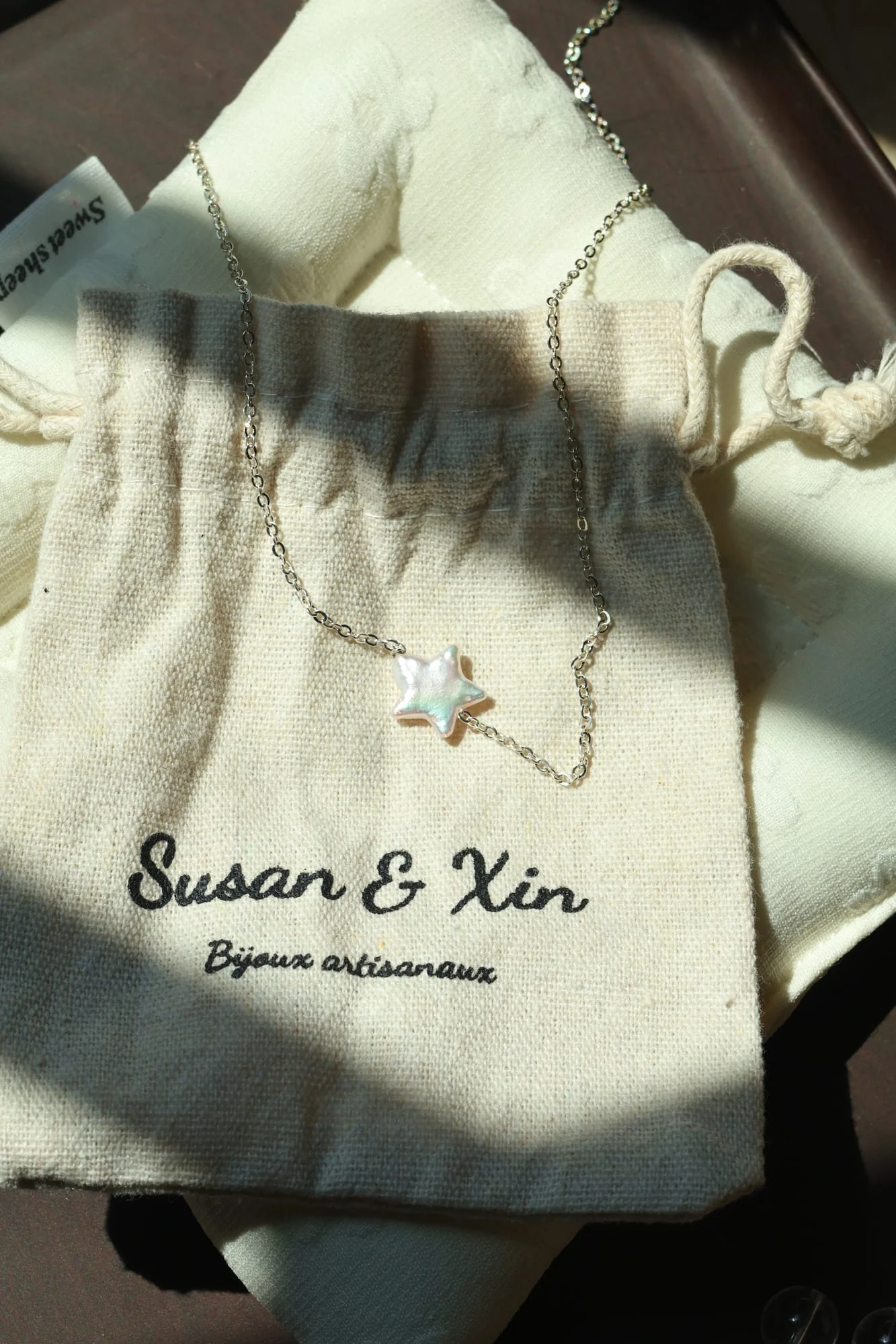 Fine silver-toned chain necklace with a single white iridescent star, resting on a Susan&Xin fabric pouch.