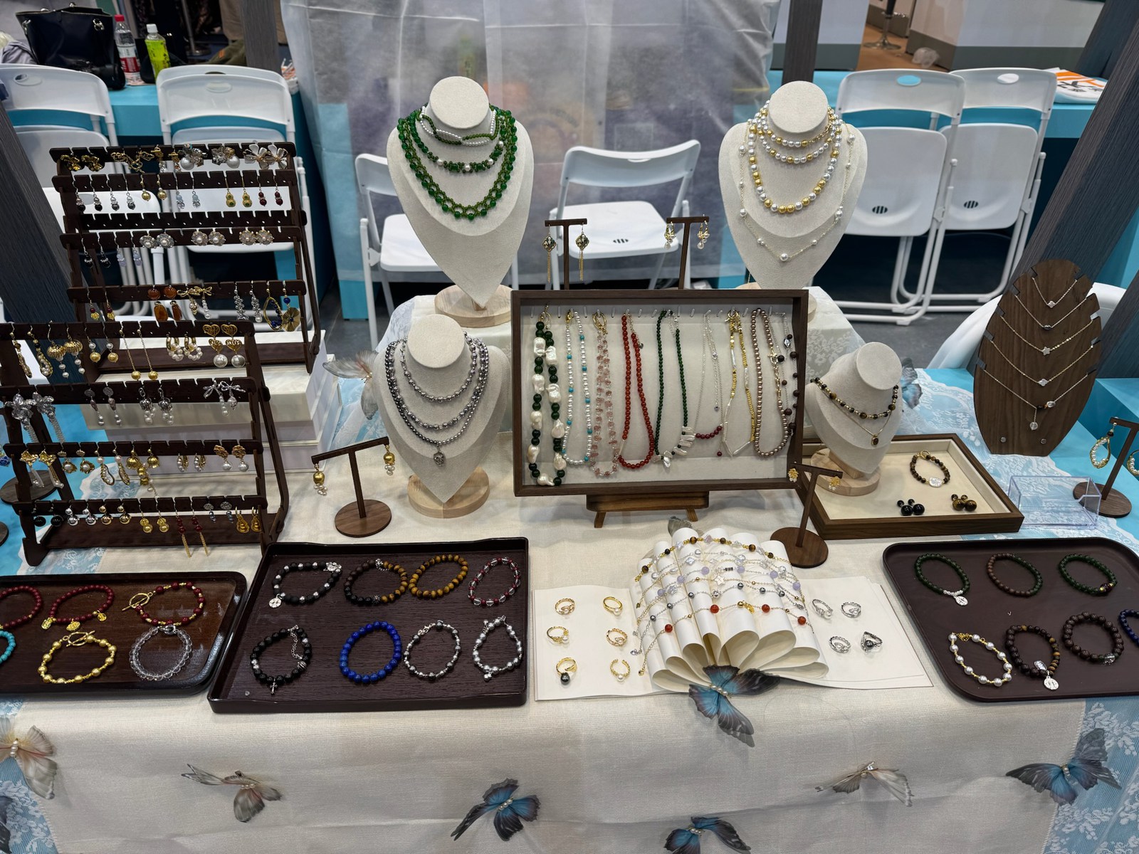 A tabletop display of necklaces, bracelets and earrings, with an open fan between the trays.