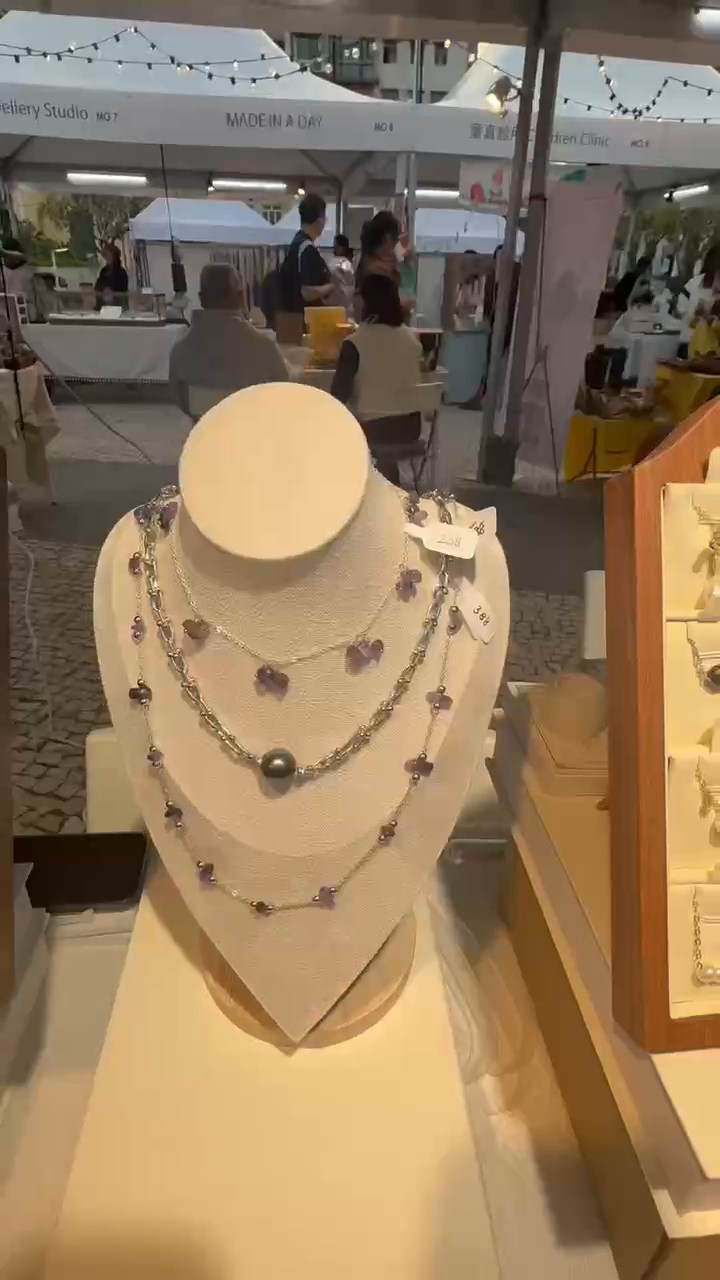 Several necklaces on a cream display bust beneath the market canopy.